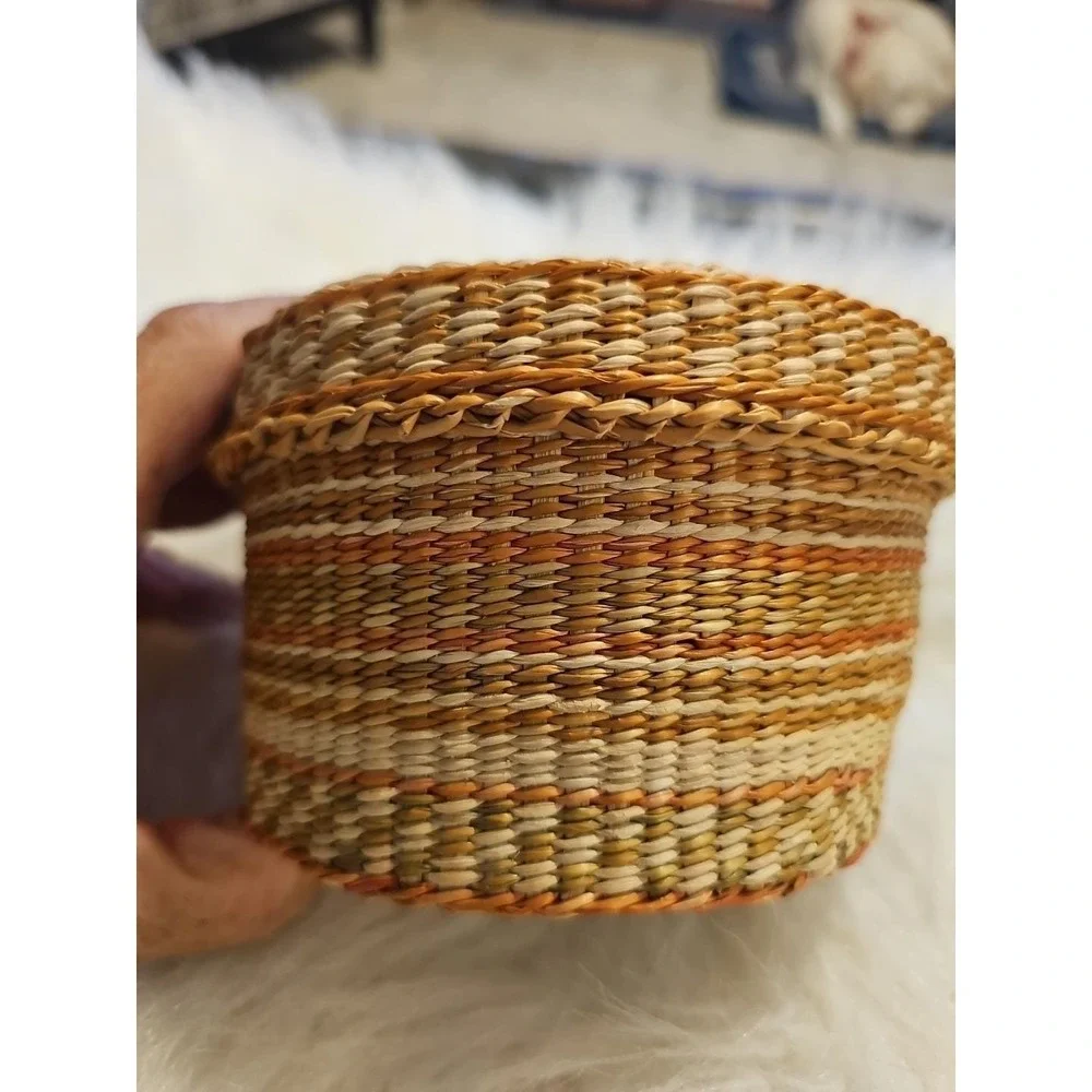 The image displays a‎ small, round, hand-woven basket with a lid, typically made